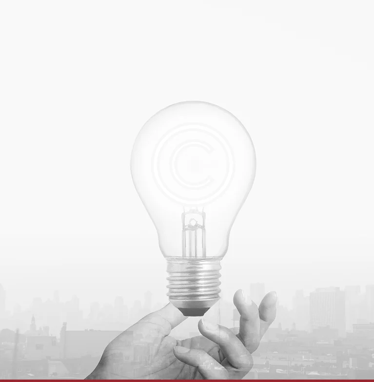 A hand holds up a lightbulb with a copyright symbol inside, against a grayscale city skyline background.