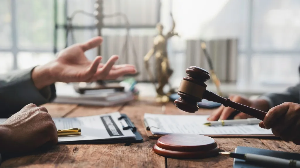 Two individuals engaged in a legal discussion with a gavel, documents, and scales of justice on a wooden table.