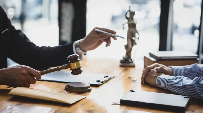 Two people at a wooden table with a judge's gavel, legal books, and a statue of Lady Justice.