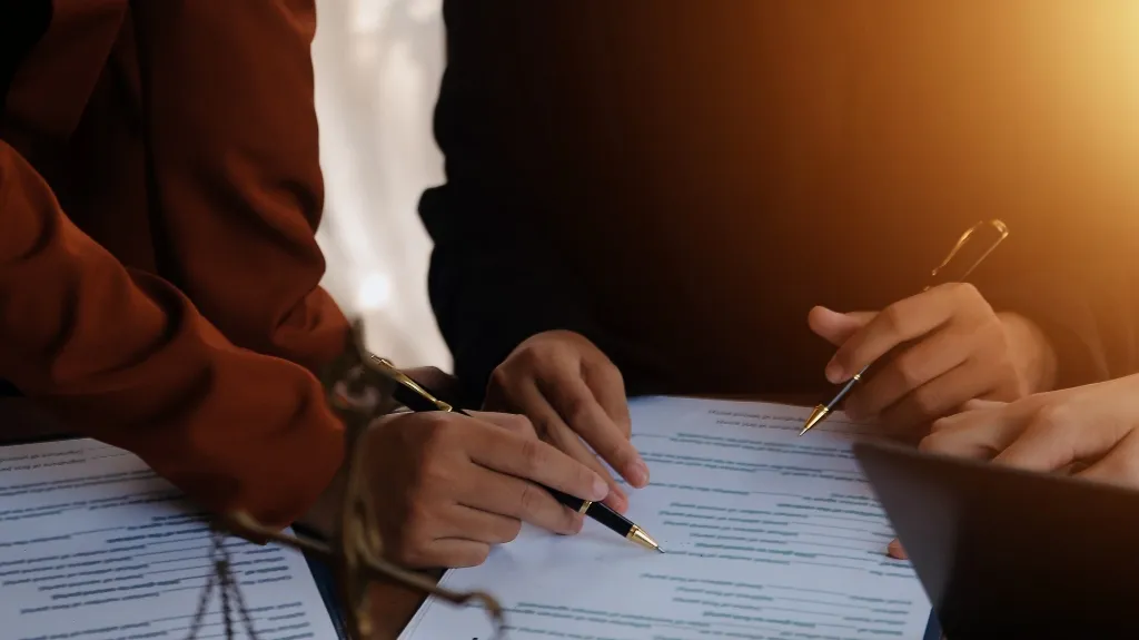 Two individuals in dark clothing reviewing and marking printed documents with pens.