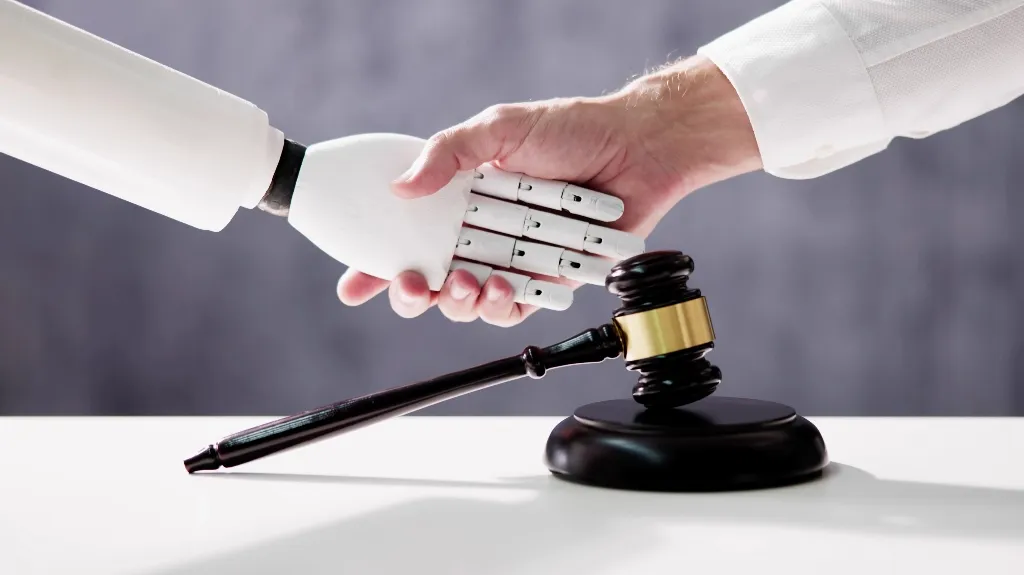 Human hand shaking a white robotic hand above a black judge's gavel on white surface.