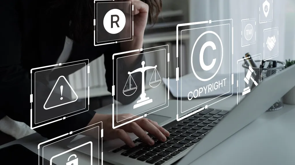 Person using laptop with translucent digital icons related to copyright and legal concepts.