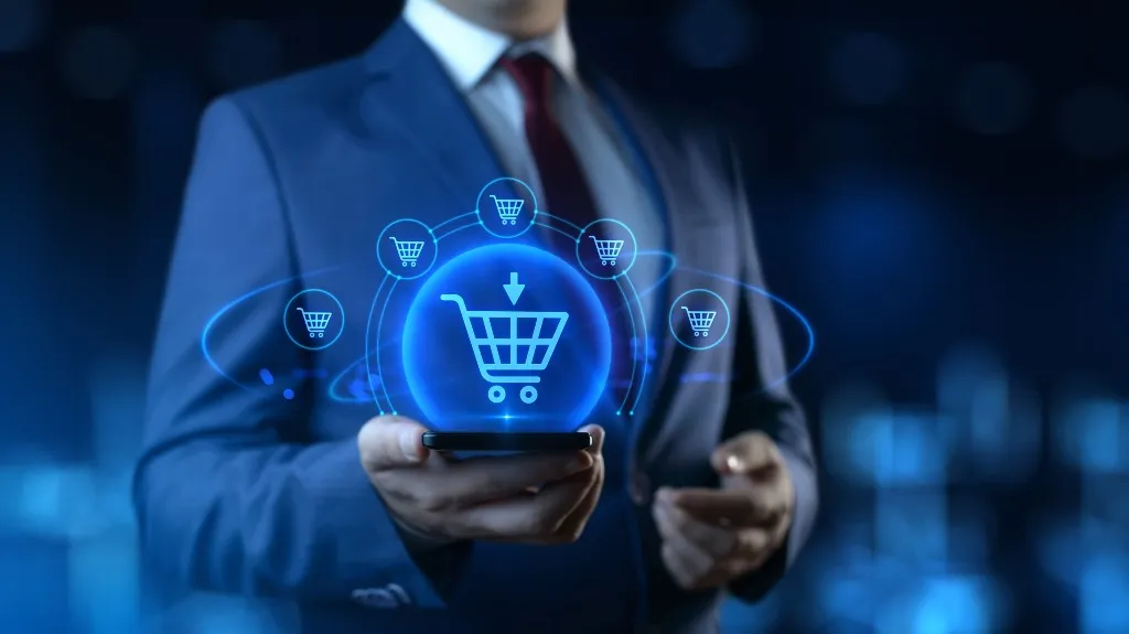 Businessman in blue suit holding smartphone with holographic shopping cart icons.