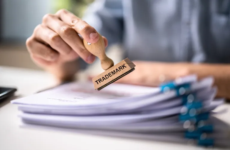 Person stamping a stack of documents with a wooden "TRADEMARK" stamp.