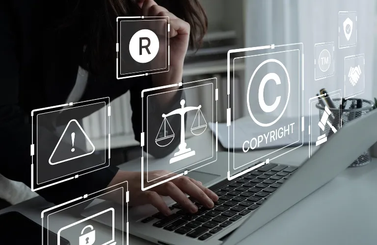 Person using laptop with floating transparent legal icons including copyright, trademark, and scales of justice.