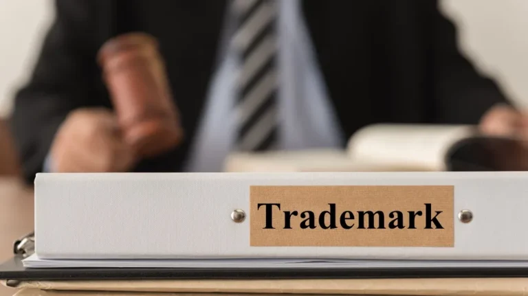 Close-up of a white binder labeled "Trademark" with a blurred person holding a gavel in the background.